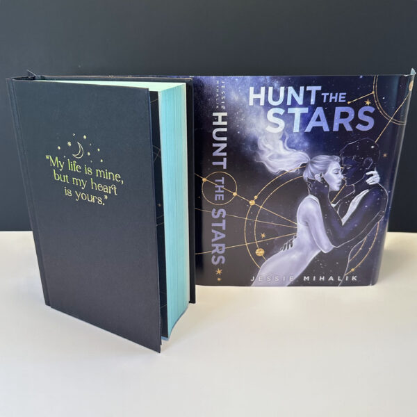 A photo of the special Bookish Box hardback edition of HUNT THE STARS with teal sprayed edges, a reversible dust jacket with a custom cover as well as the original artwork, and an embossed quote on the front of the book.